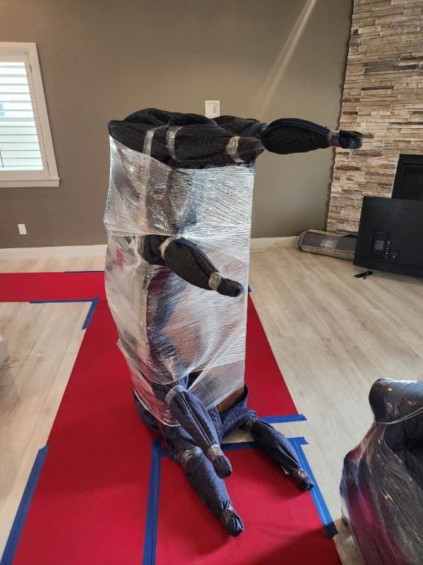 Tall clock fully wrapped in pads and shrink wrap on red floor runners