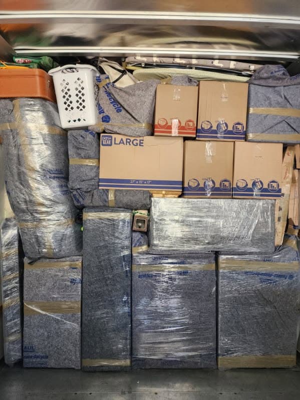 A dense sealed wall of padded, shrink-wrapped furniture and boxes in a truck